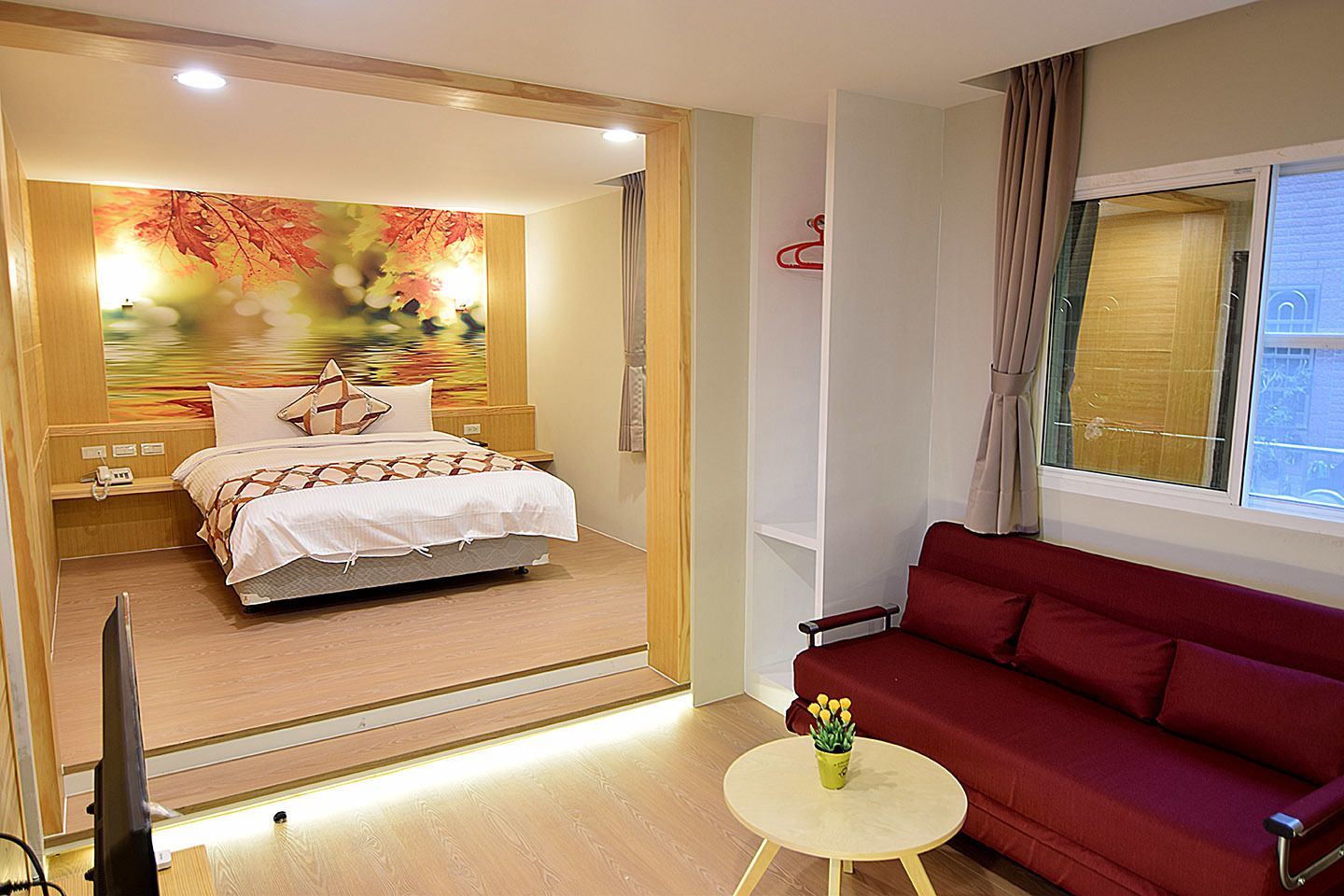 Ett hotellrum med en säng, en röd soffa, ett litet bord med blommor och en tavla på väggen.