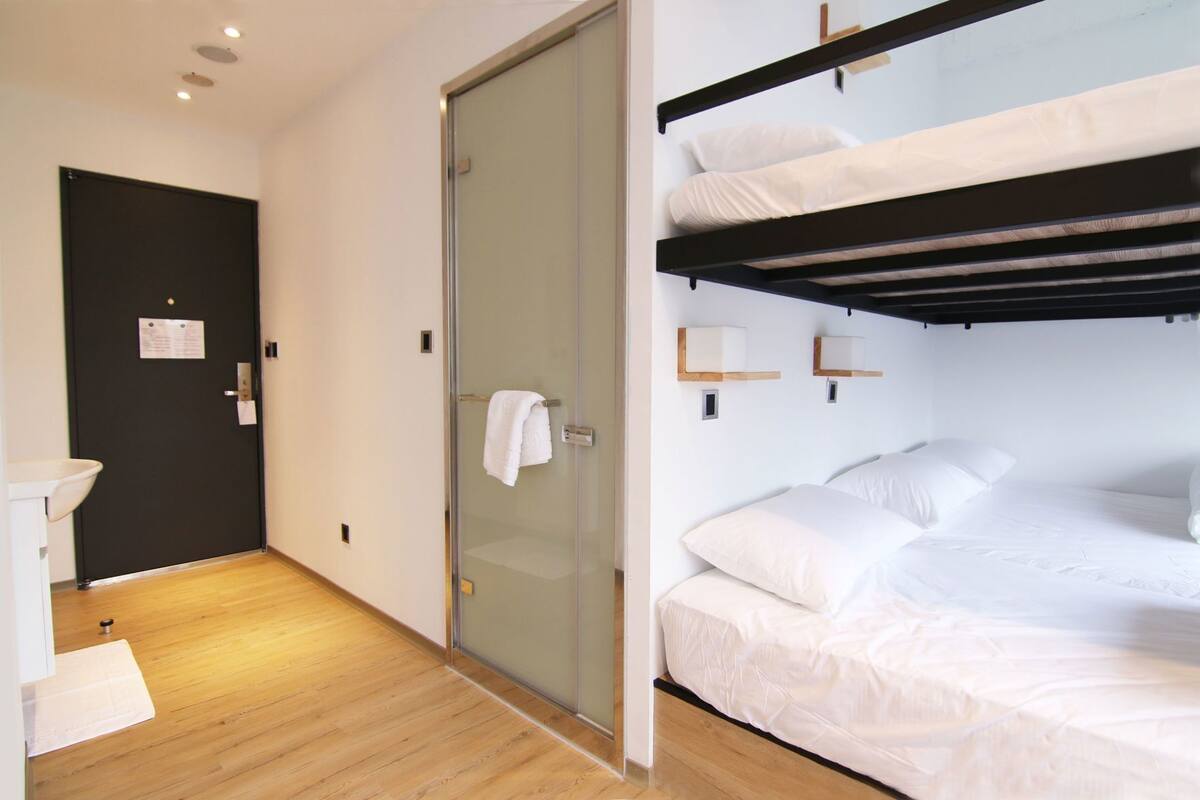 Ein Hotelzimmer mit einem Etagenbett, einer Glastür, einem weißen Waschbecken und Holzboden.