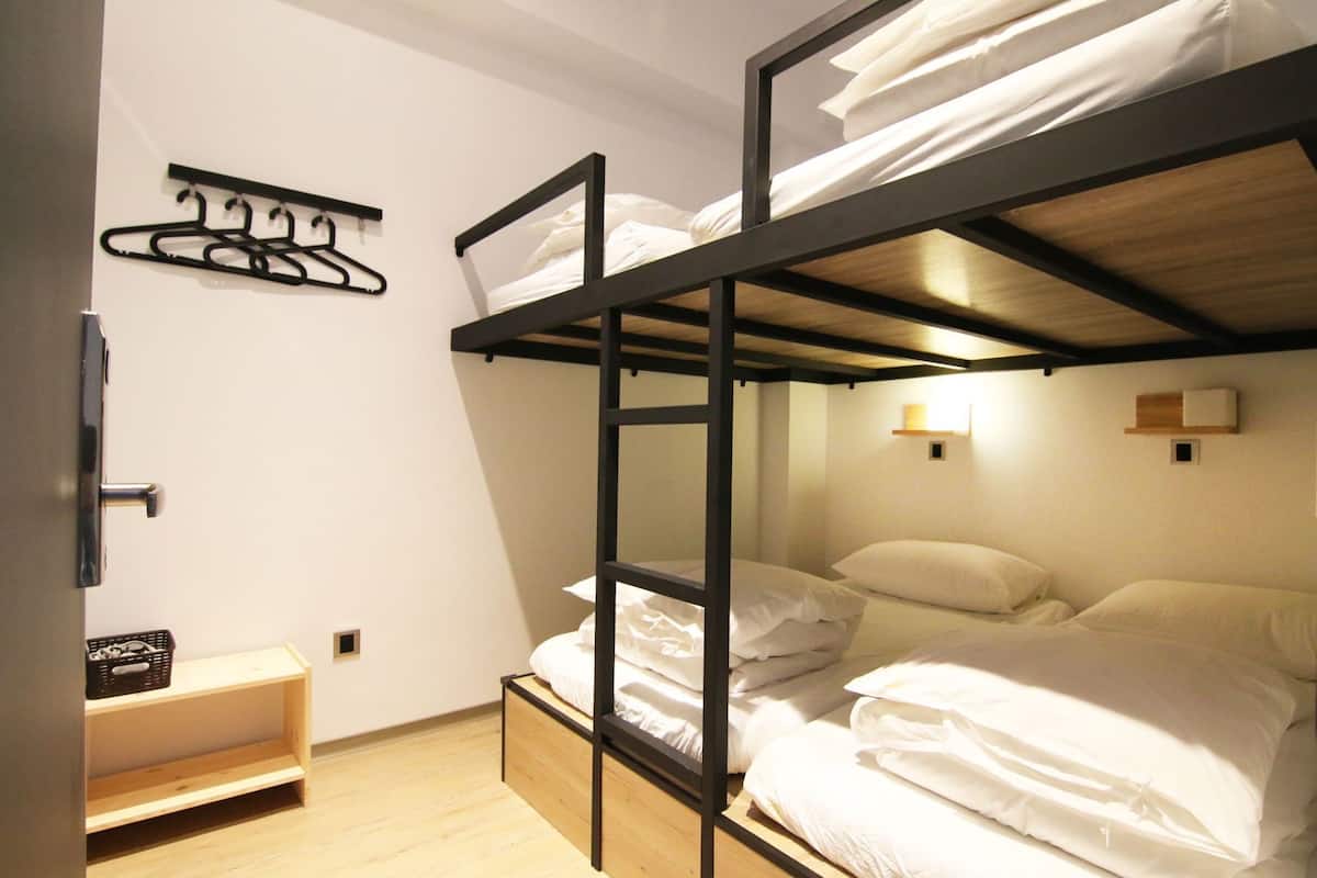 Ein Schlafraum mit Etagenbetten, Holzboden, Wandgarderobe und einem kleinen Nachttisch.