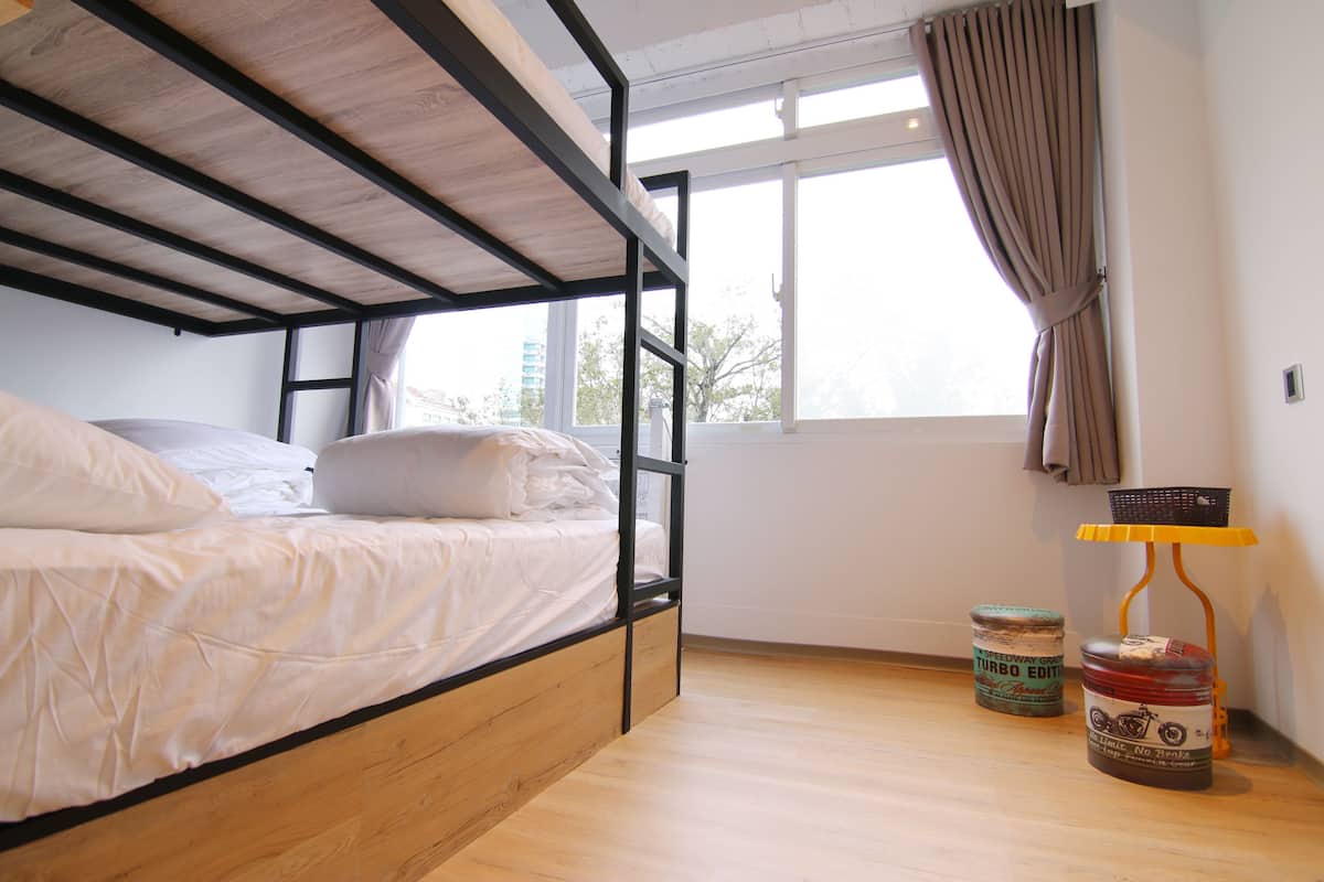 Ein Stockbett in einem Zimmer mit Holzboden, einem mit Vorhängen versehenen Fenster und zwei Vintage-Behältern auf dem Boden.