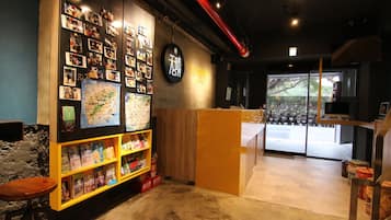 A cozy hostel interior with a wall decorated with photos, a wooden reception desk, and a view of the street outside.