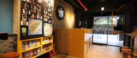 A cozy hostel interior with a wall decorated with photos, a wooden reception desk, and a view of the street outside.