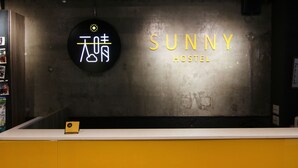 Uma receção com um letreiro de néon a dizer "SUNNY HOSTEL" e outro letreiro com caracteres chineses.