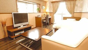 Una habitación de hotel con televisión, escritorio, silla, cama y ventana con cortinas.
