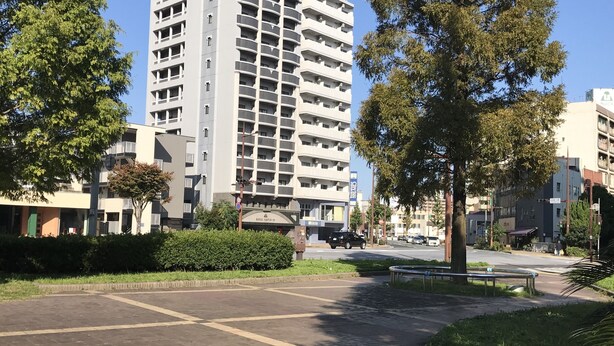 Un edificio de varios pisos con balcones, rodeado de árboles y un área pavimentada.