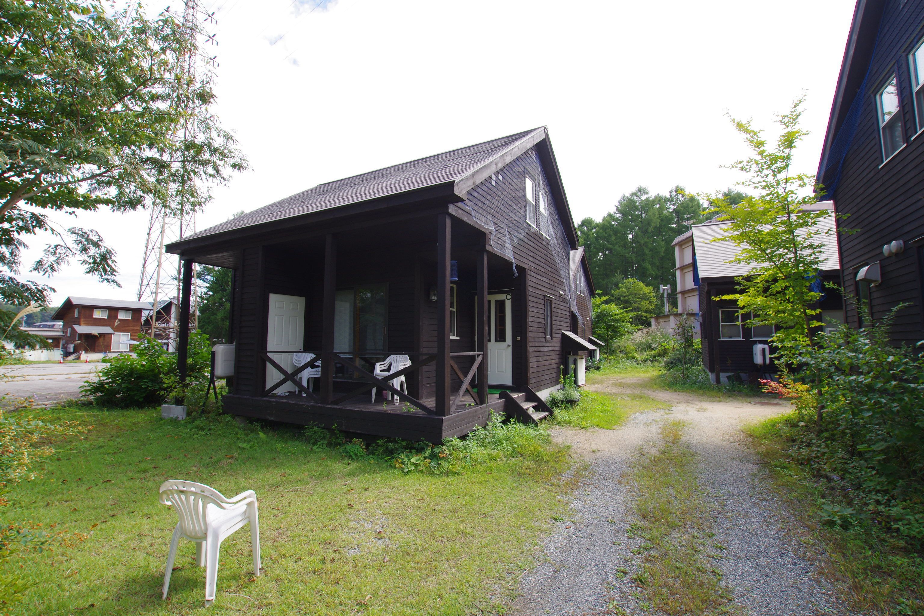 A rustic cabin with a porch, a gravel path leading to it, and a white plastic chair in the foreground.