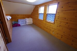 A small attic room with wooden walls, a sloped ceiling, and two windows with patterned glass.
