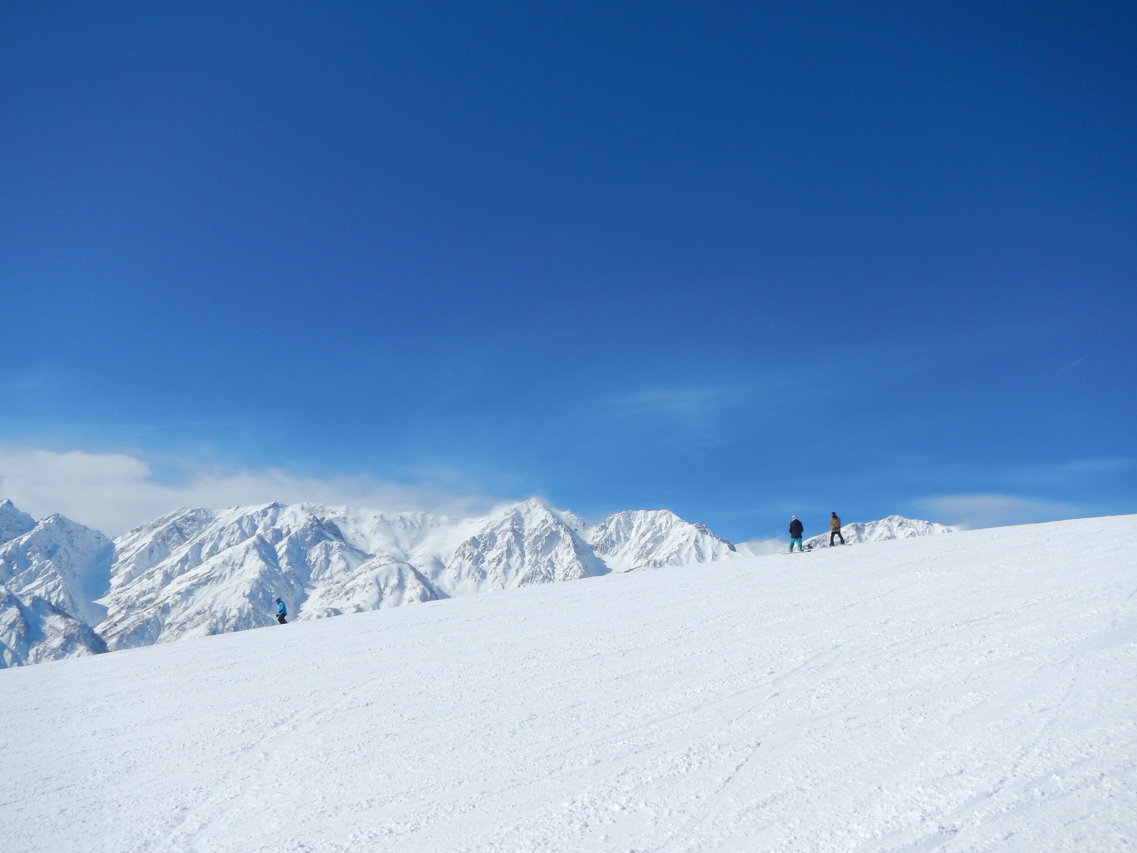 A snowy mountain landscape with two skiers on a slope.