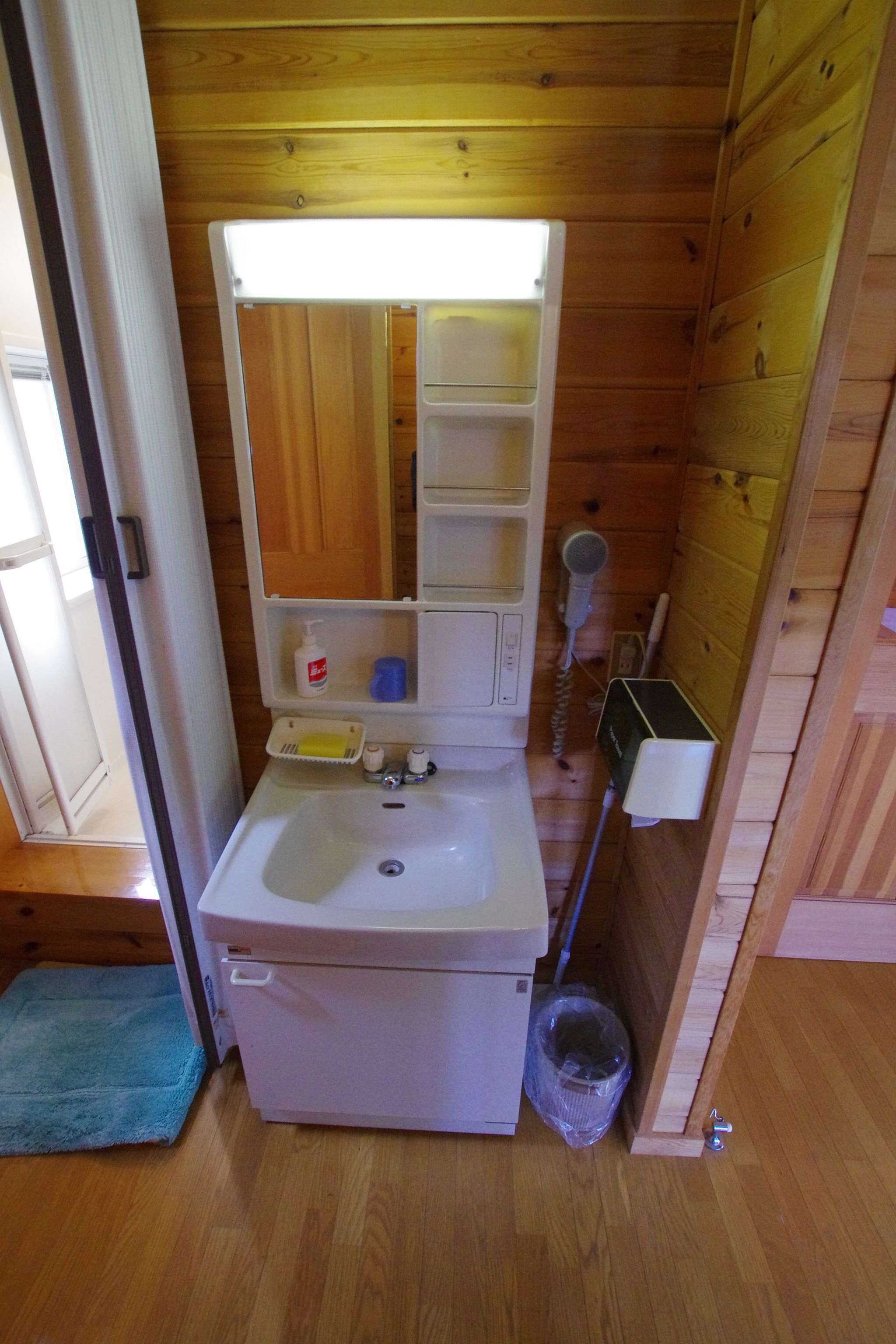 A compact bathroom with a white sink, a mirror, and a small shelf with toiletries.