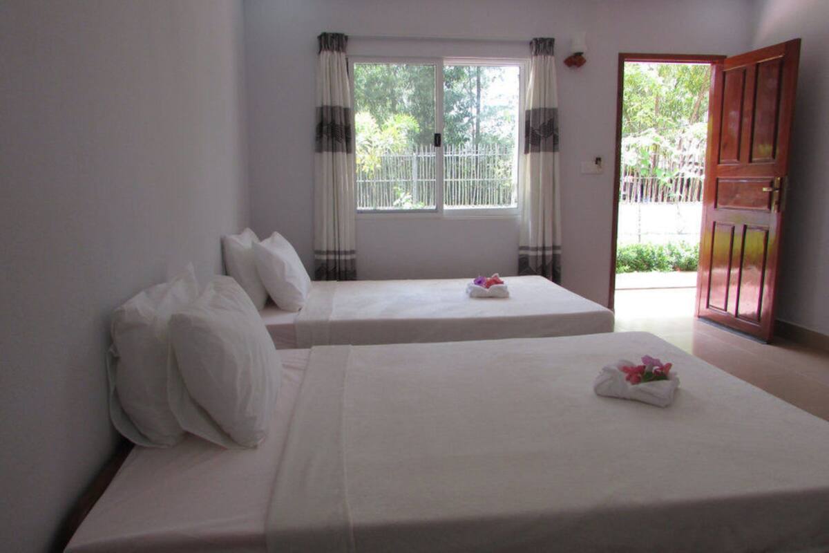 Una habitación con dos camas, una ventana con cortinas y una puerta que da al exterior.
