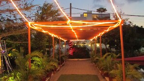 Un espace extérieur abrité, doté d’un chemin, et entouré de plantes en pot et d’arbres.