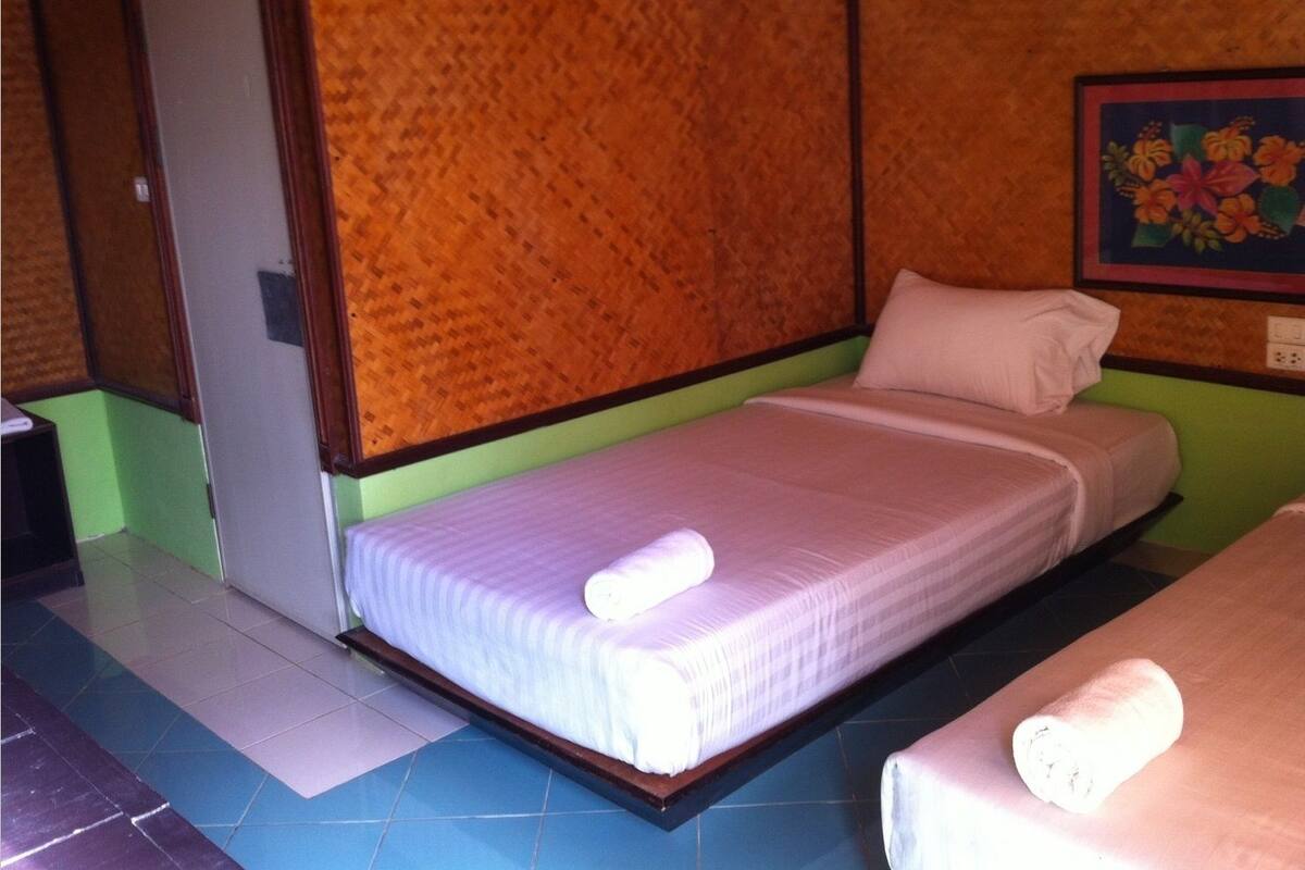 A single bed with a white mattress and pillow, a wooden headboard, and a wall with a floral painting.