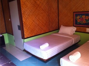 Una cama individual con colchón y almohada blancos, cabecera de madera, y una pared con un cuadro floral.