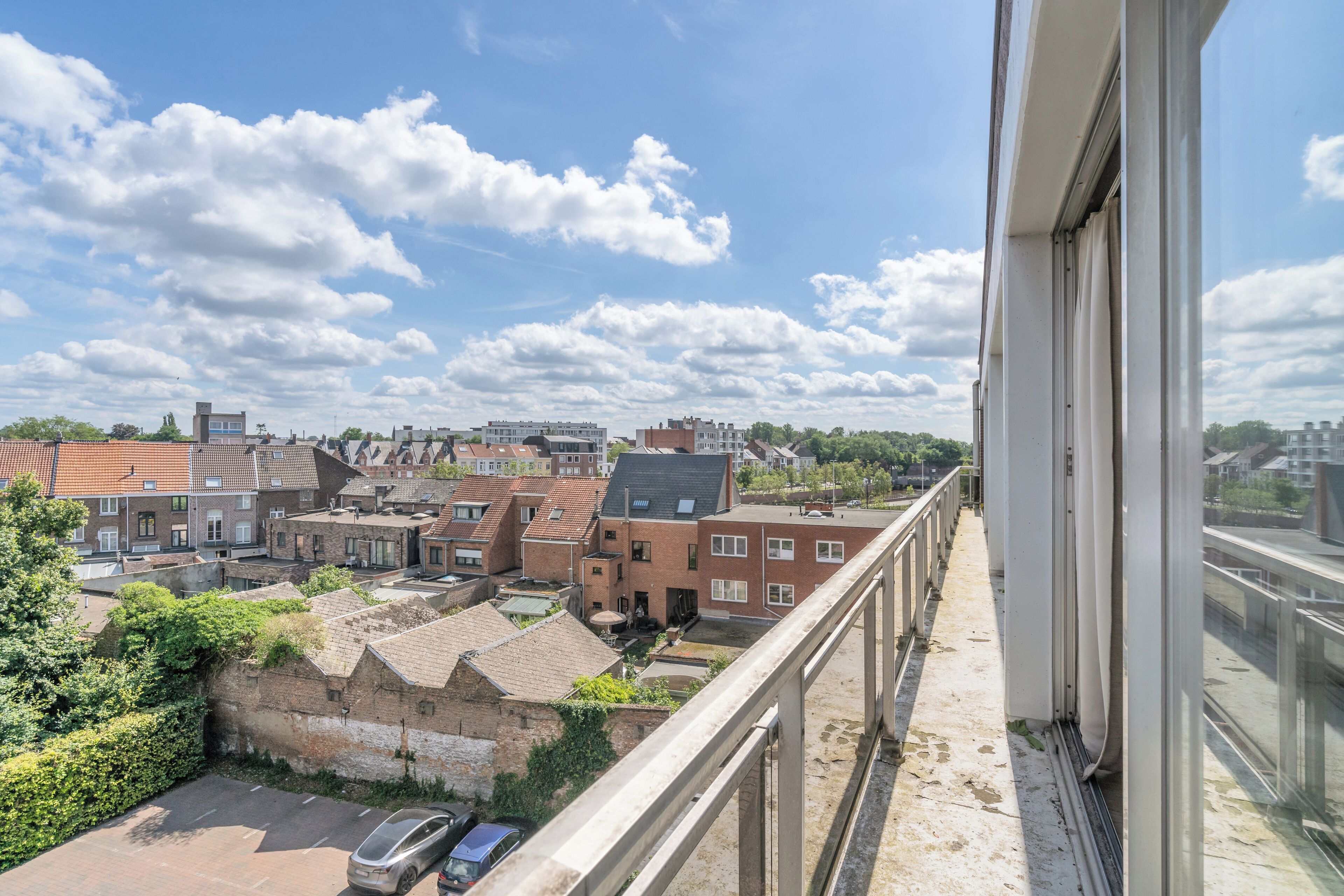 A balcony with a view of a residential area, including houses and parked cars.