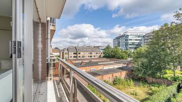 Un balcón con vista a un paisaje urbano, que incluye un edificio moderno y una construcción de ladrillo.