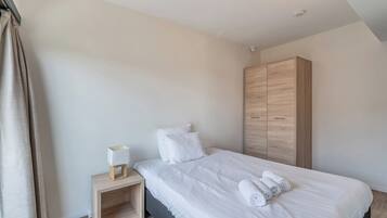 Um quarto moderno com uma cama grande, um guarda-roupa de madeira, uma mesa de cabeceira com abajur e toalhas dobradas com cuidado.