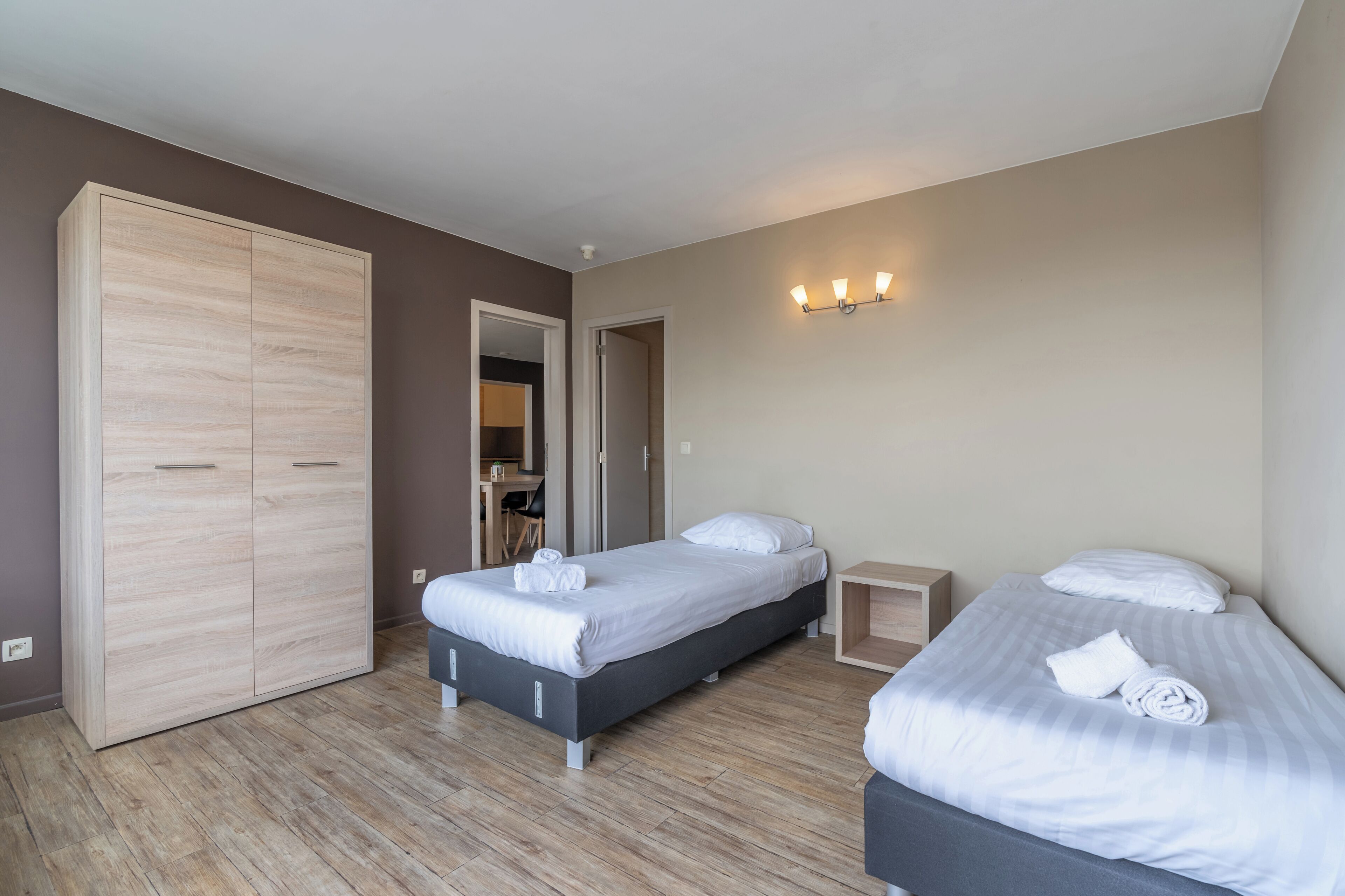 A hotel room with two beds, a wardrobe, a desk, and a bathroom.