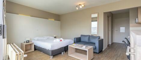 Una habitación de hotel moderna con cama, sofá, una mesita de centro de madera y una mesita de noche pequeña con lámpara.