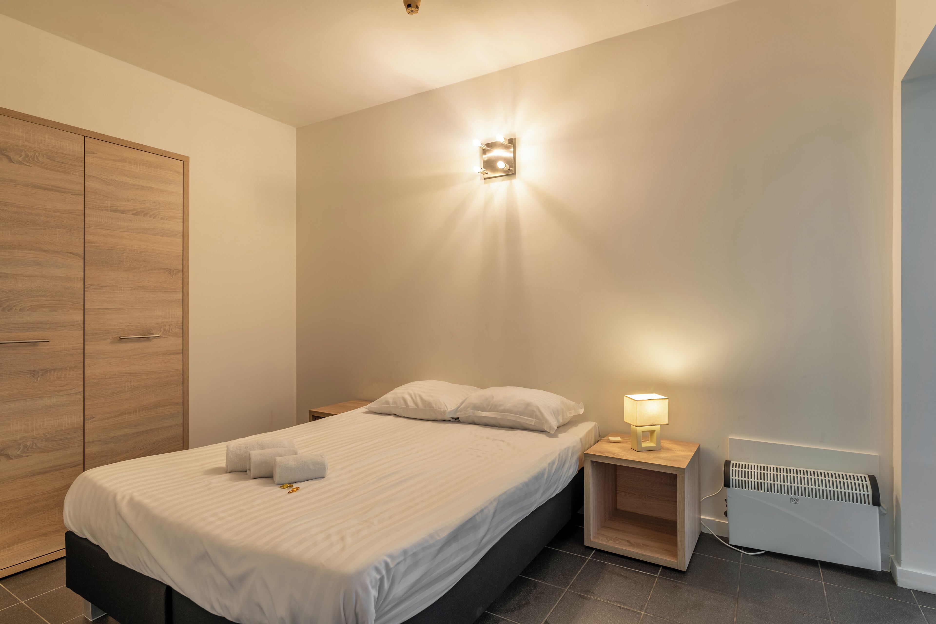 Une chambre à coucher comprenant un lit, des tables de chevet, une lampe fixée au mur et un radiateur.