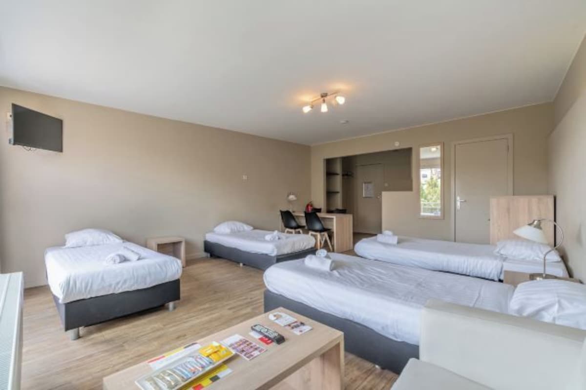 Habitación de hotel con tres camas, un escritorio, una silla y un televisor.
