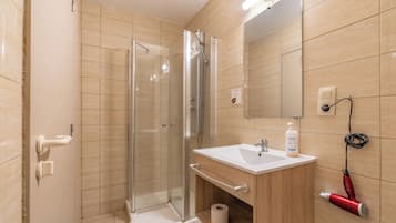 A bathroom with a glass shower enclosure, a sink with a mirror, and a hairdryer on the wall.