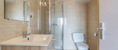 Un baño moderno con tocador de madera, cabina de ducha con vidrio y inodoro blanco.