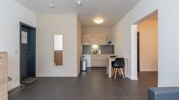 A modern kitchen with dark tiles, a dining area with a black chair, and a small refrigerator.
