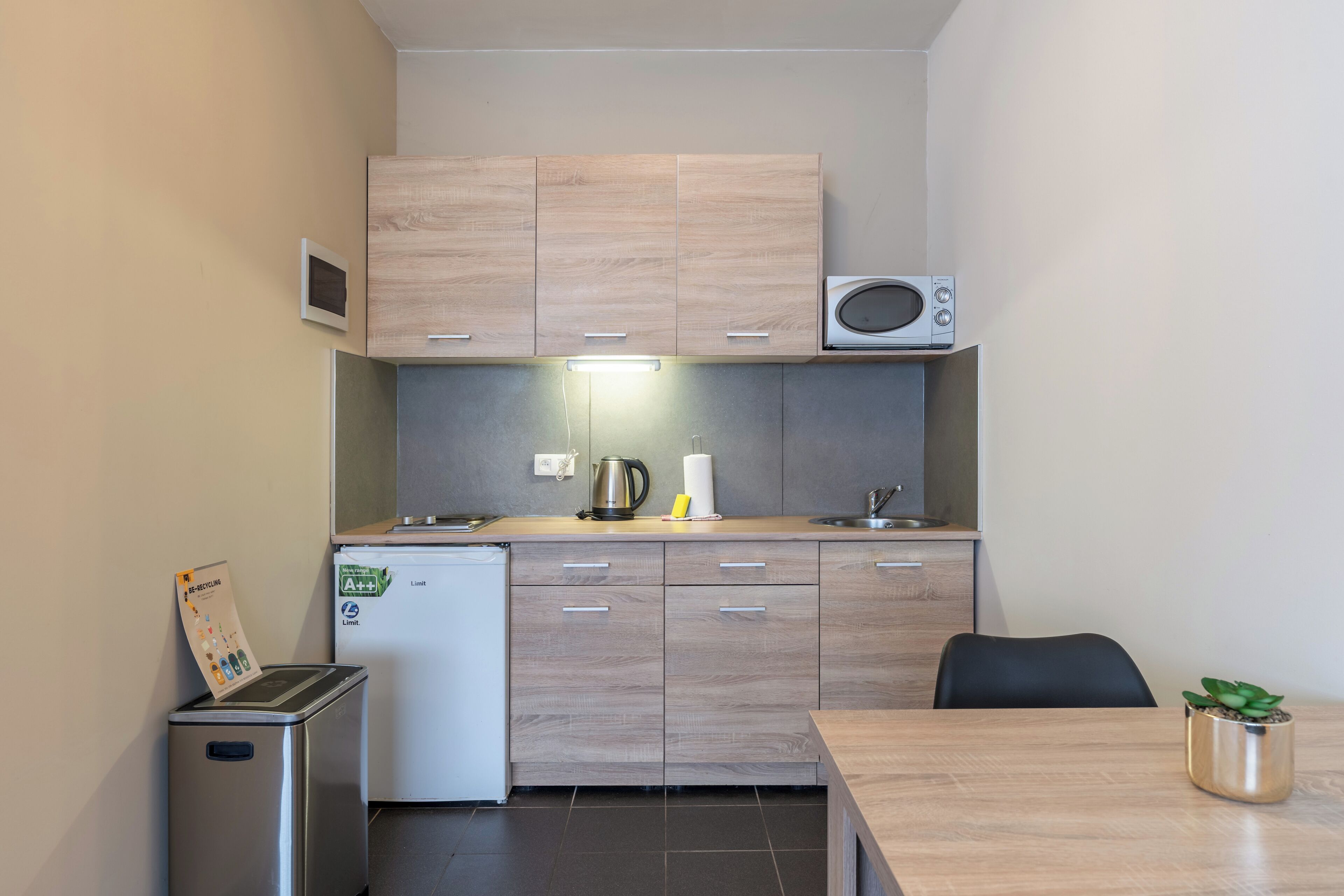 A compact kitchenette with a microwave, a small refrigerator, and a trash bin.