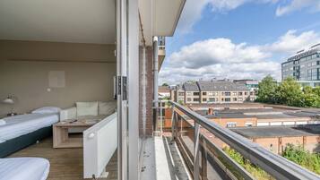 A balcony with a view of the cityscape, a bed, a small table, and a radiator.
