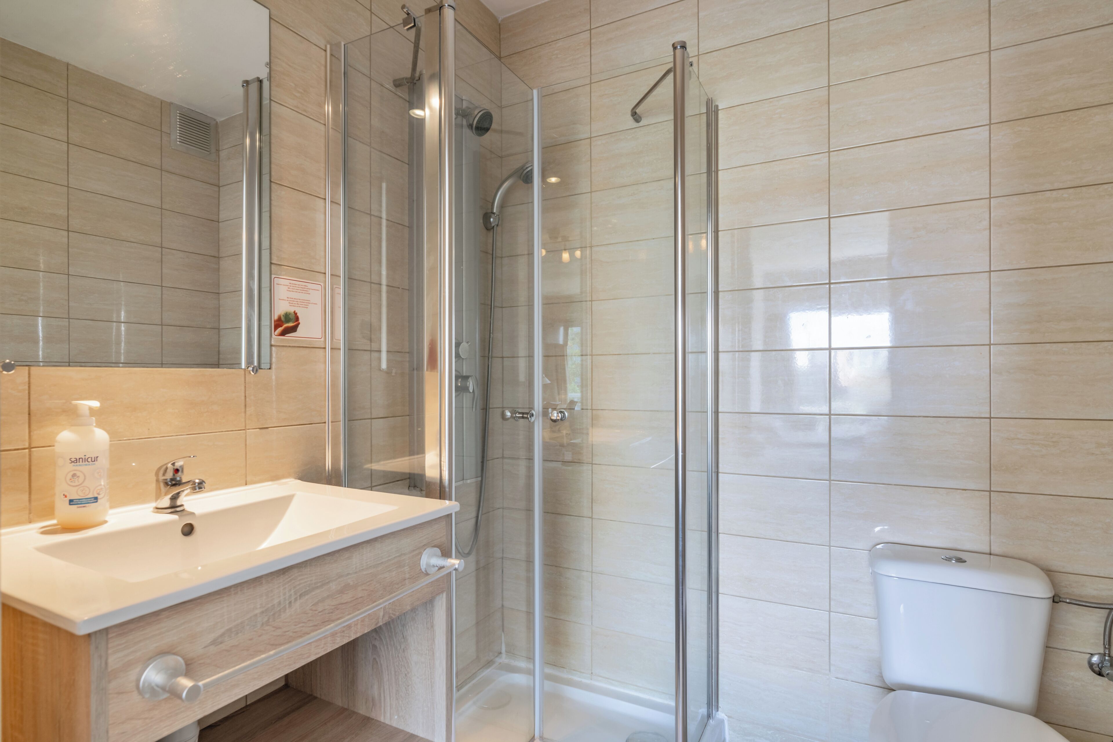 Een moderne badkamer met een douchecabine van glas, een wastafel met spiegel en een toilet.