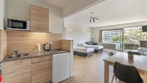 A modern kitchen with a microwave, sink, and refrigerator. There is a dining area with a table and chairs. The room has large windows with a view of buildings and trees. - Value Stay Residence Mechelen (Mechelen)