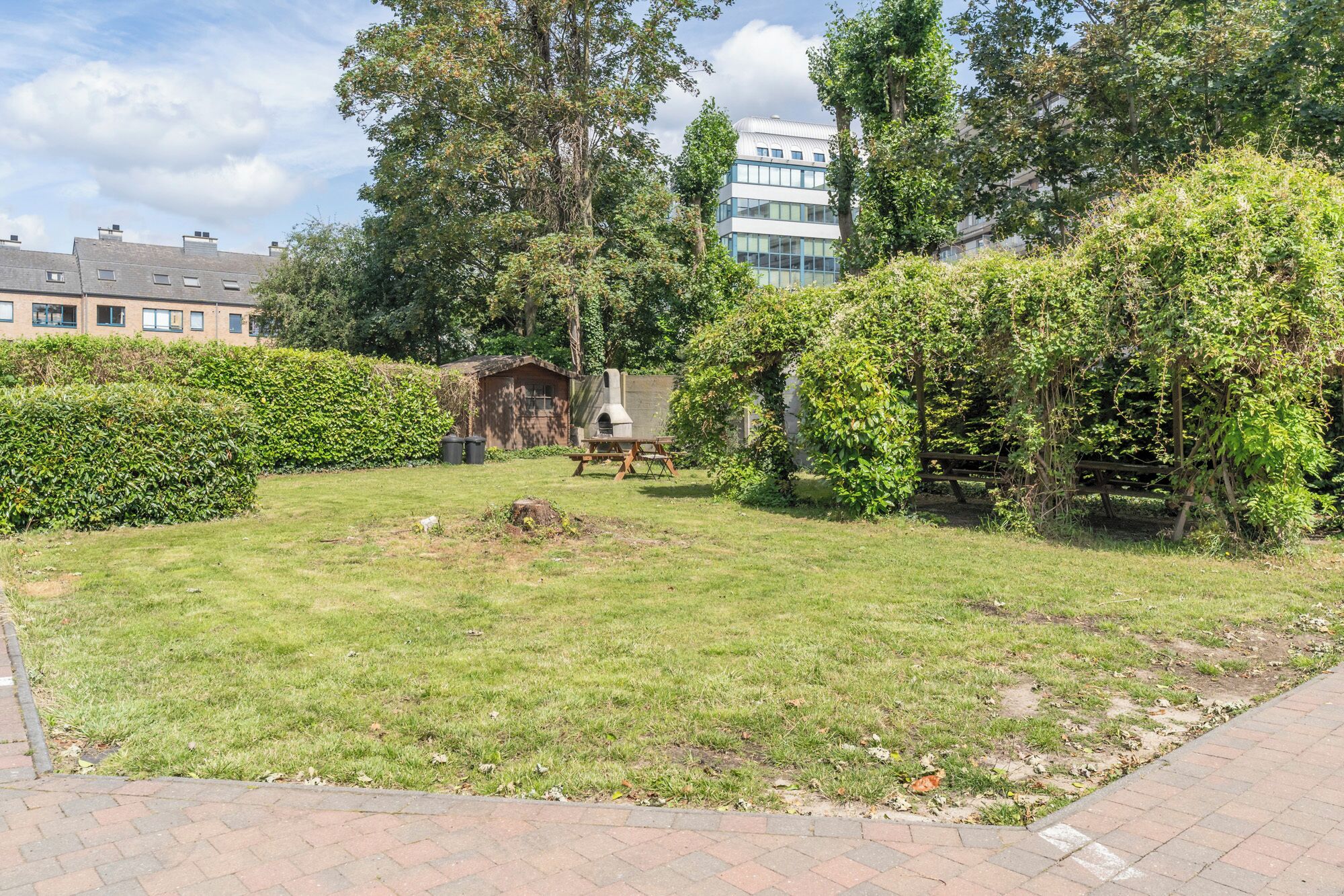 Un patio con césped, una mesa de picnic, una estructura de piedra y un edificio al fondo.