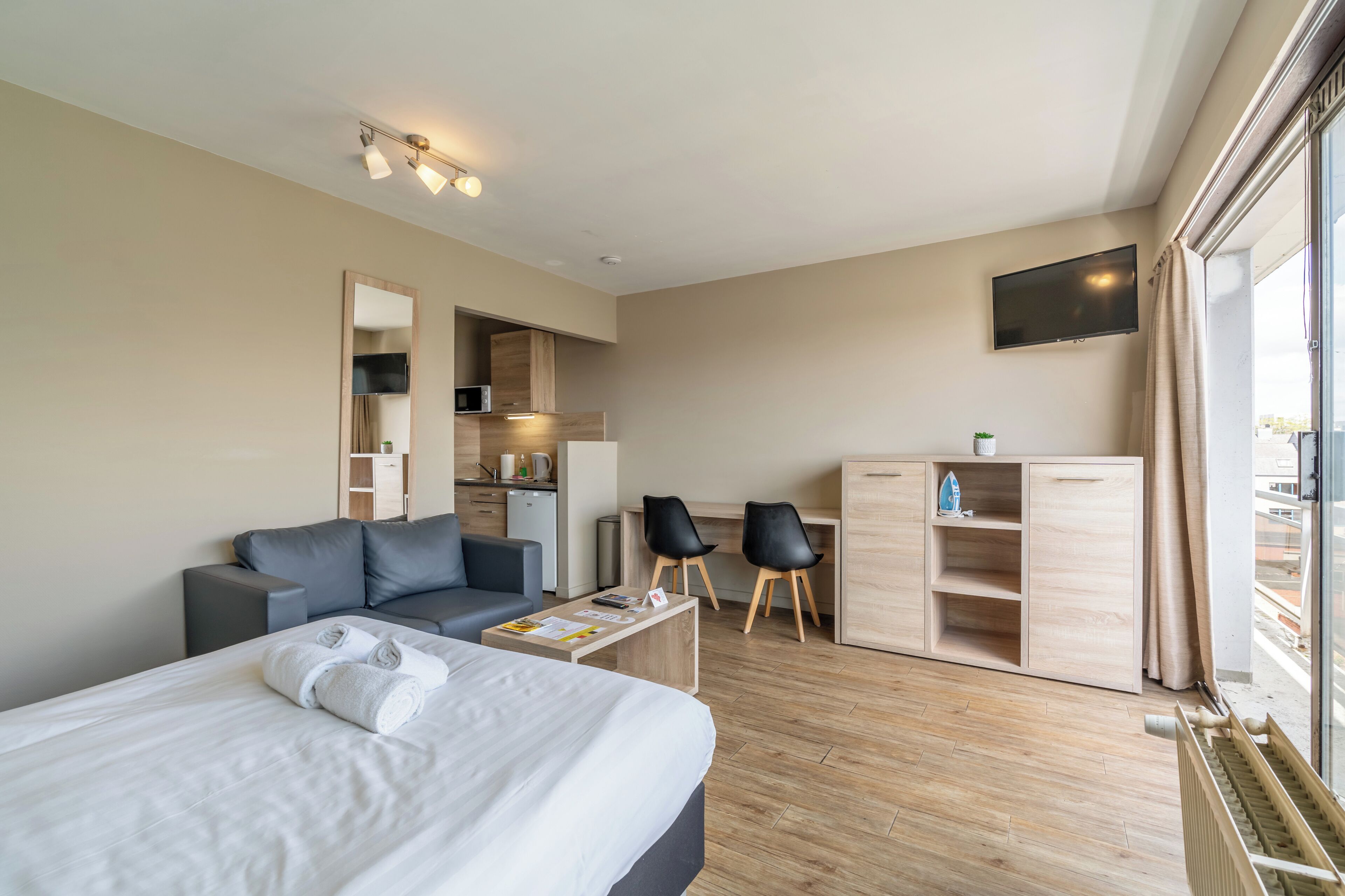 A modern hotel room with a bed, a sofa, a desk, and a TV.