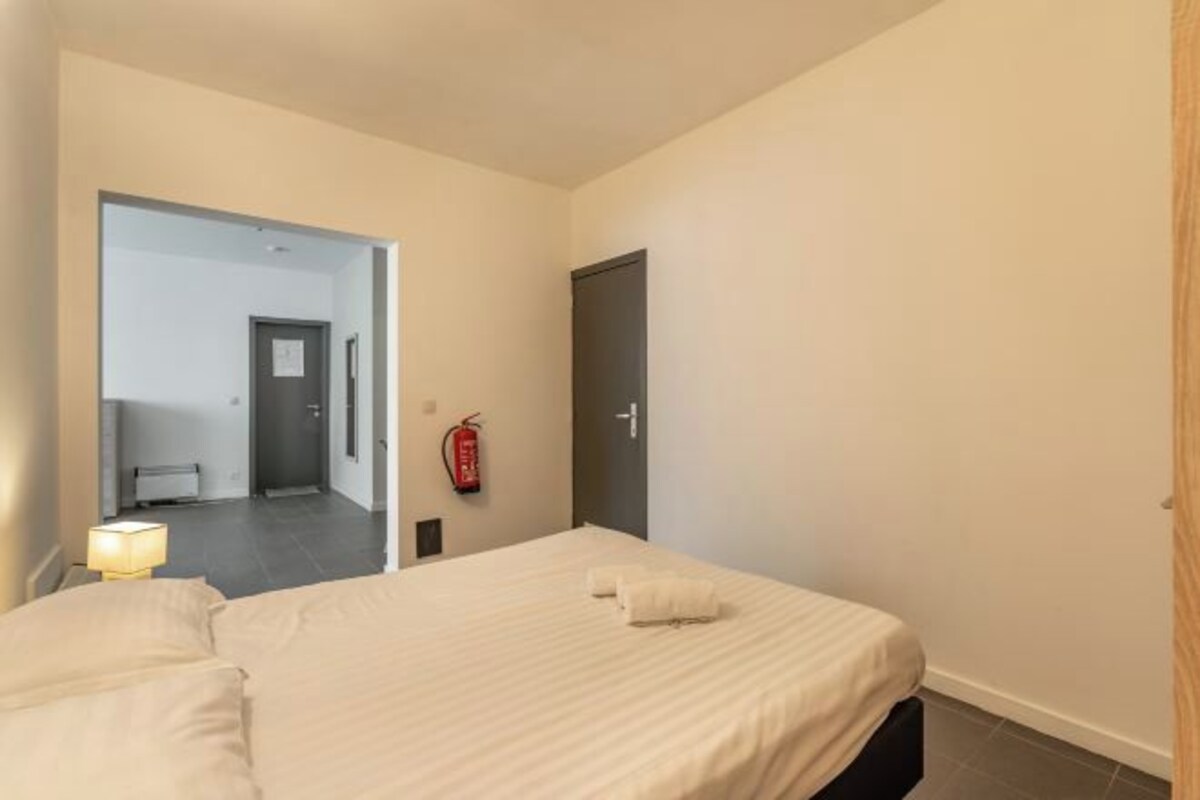 Habitación de hotel con cama, lámpara de noche, extintor y puerta que da a un baño.