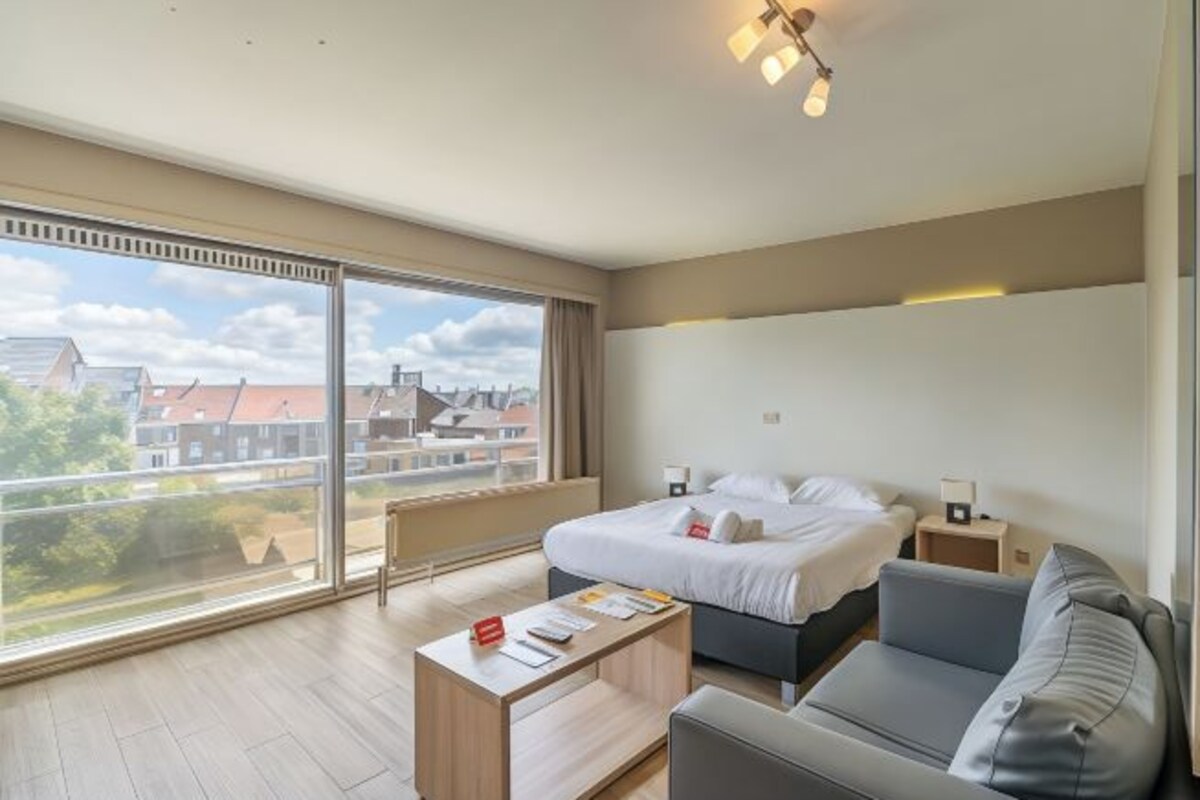 Una habitación de hotel moderna con un ventanal grande, una cama, un sofá y una mesita.