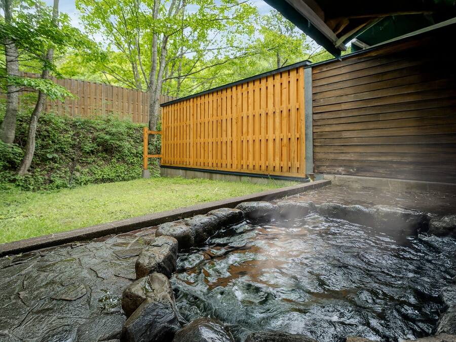 A hot spring area with a wooden fence, a stone pathway, and a wooden building.