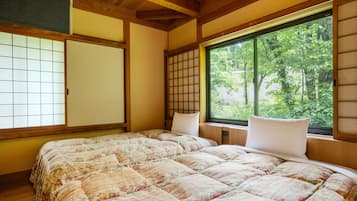 A traditional Japanese-style room with tatami flooring, a shoji screen, a large window with a view of greenery, and a bed with floral bedding.