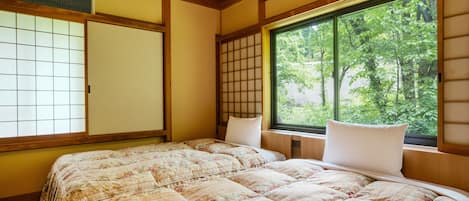 A traditional Japanese-style room with tatami flooring, a shoji screen, a large window with a view of greenery, and a bed with floral bedding.