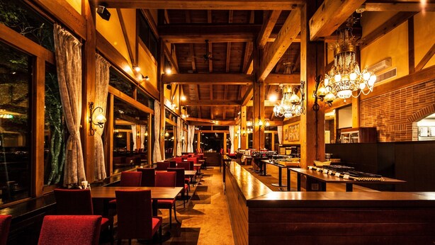Ein Restaurant mit Holzbalken, Kristalllüstern und rot gepolsterten Stühlen.