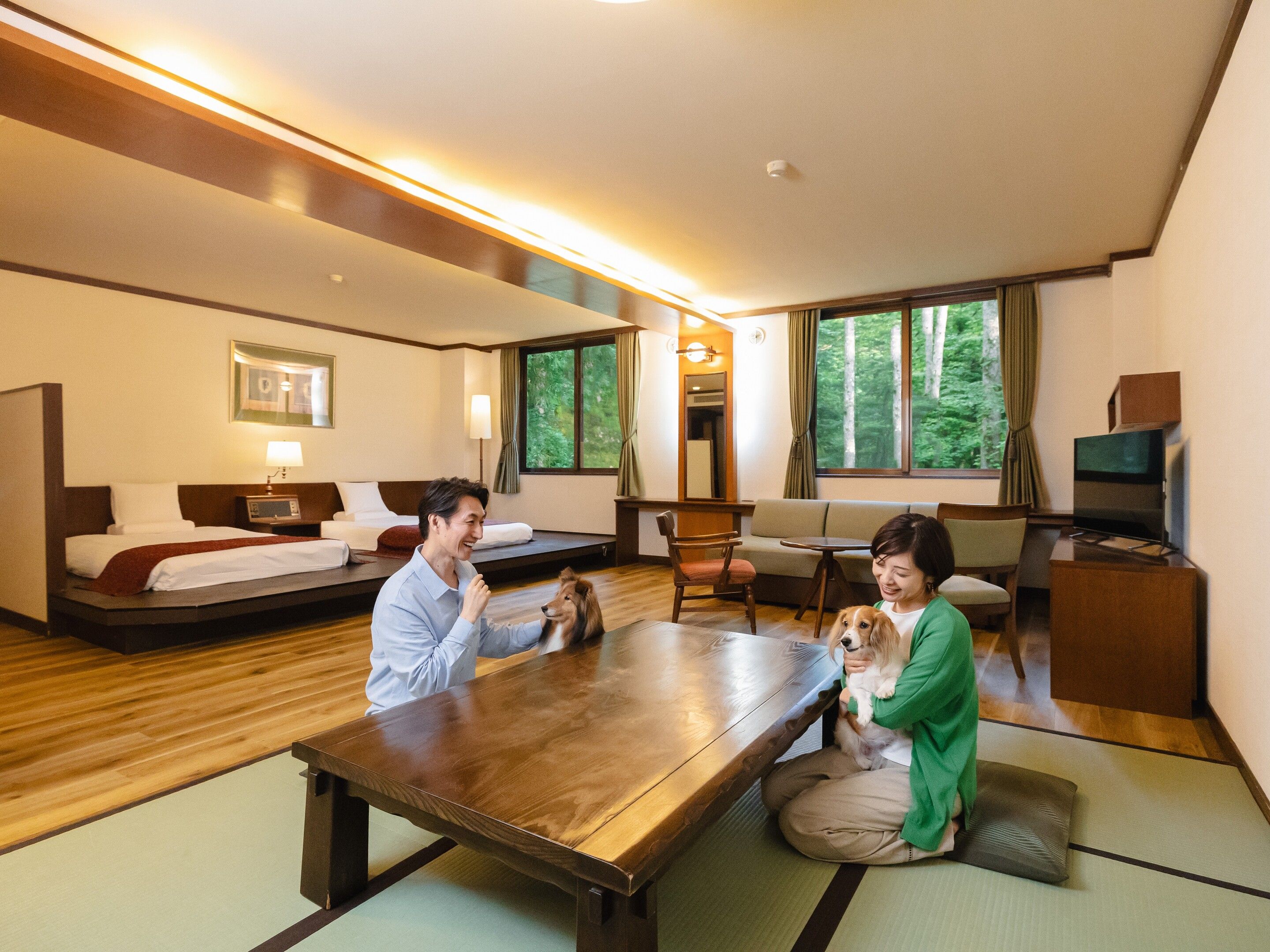 A hotel room with a bed, sofa, dining table, and a TV.