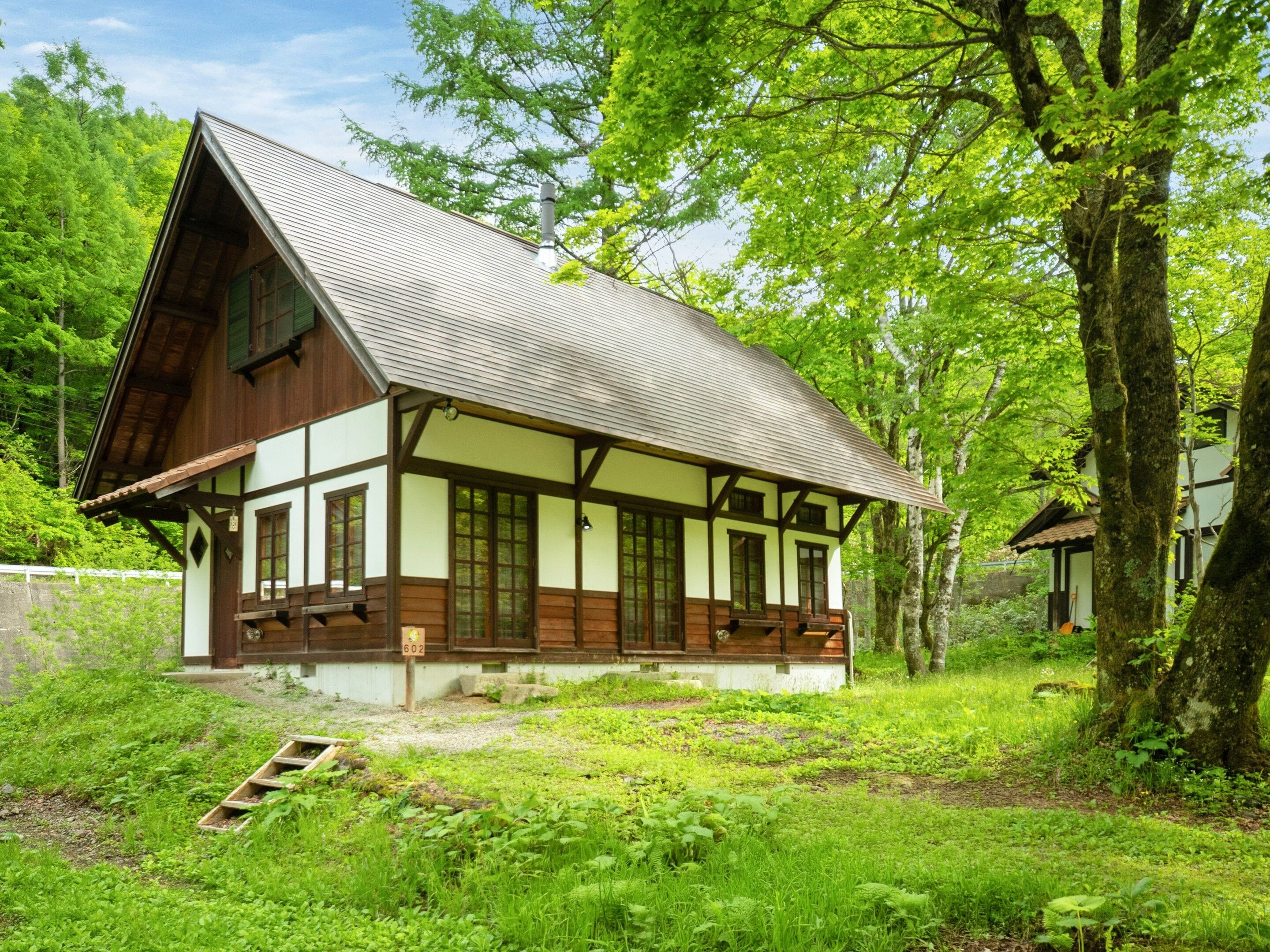 A traditional half-timbered house with a sloped roof, surrounded by lush greenery and trees.