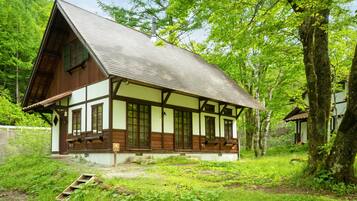 A traditional half-timbered house with a sloped roof, surrounded by lush greenery and trees.