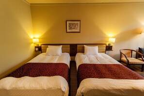 A hotel room with two single beds, each with a red patterned bedspread and white pillows. There are two bedside lamps, a framed picture on the wall, and a chair with a striped cushion. - Wan Wan Paradise Takayama (Takayama)