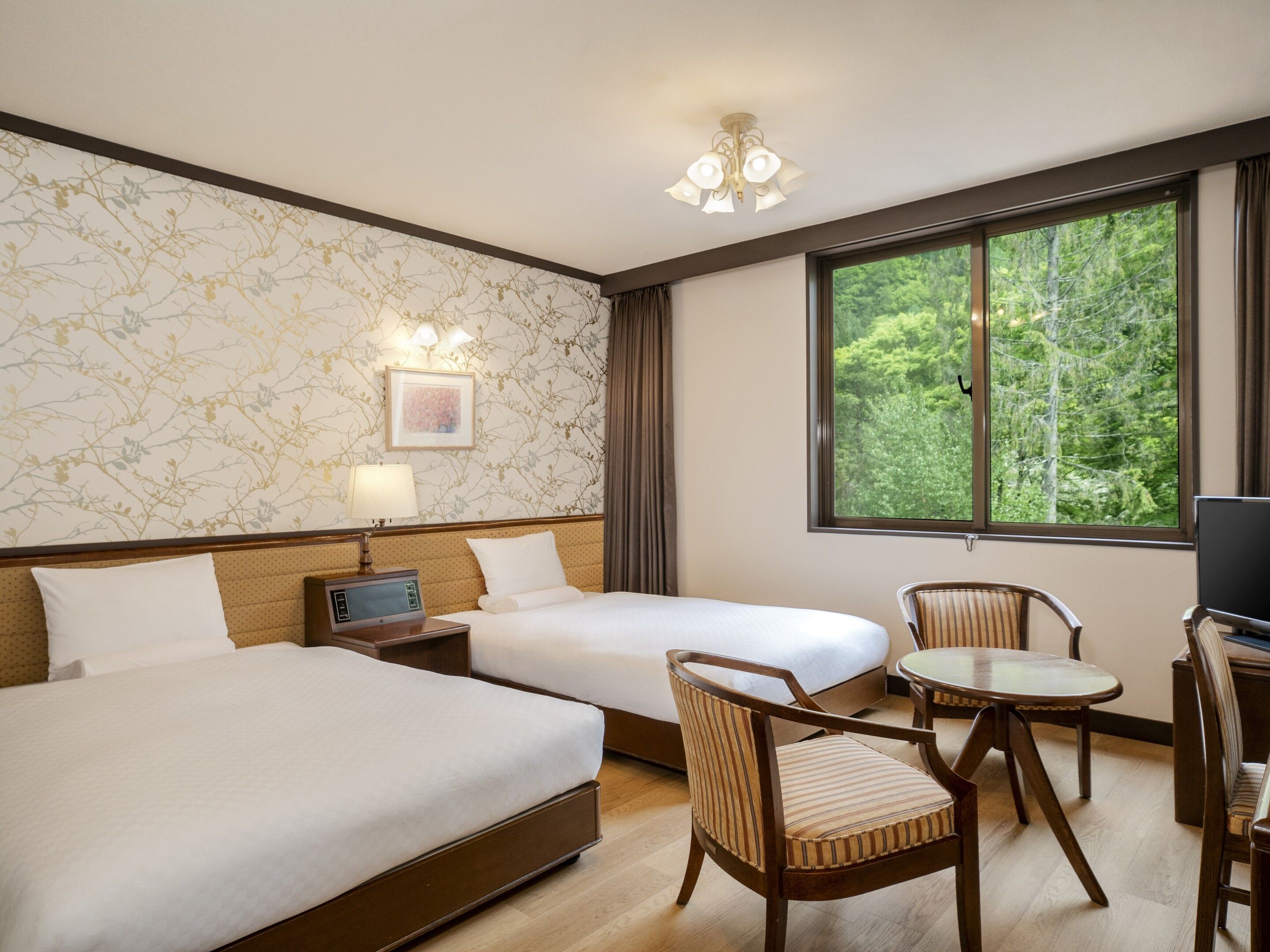 Une chambre d’hôtel avec deux lits, un bureau, une chaise, une télévision et une fenêtre donnant sur la forêt.
