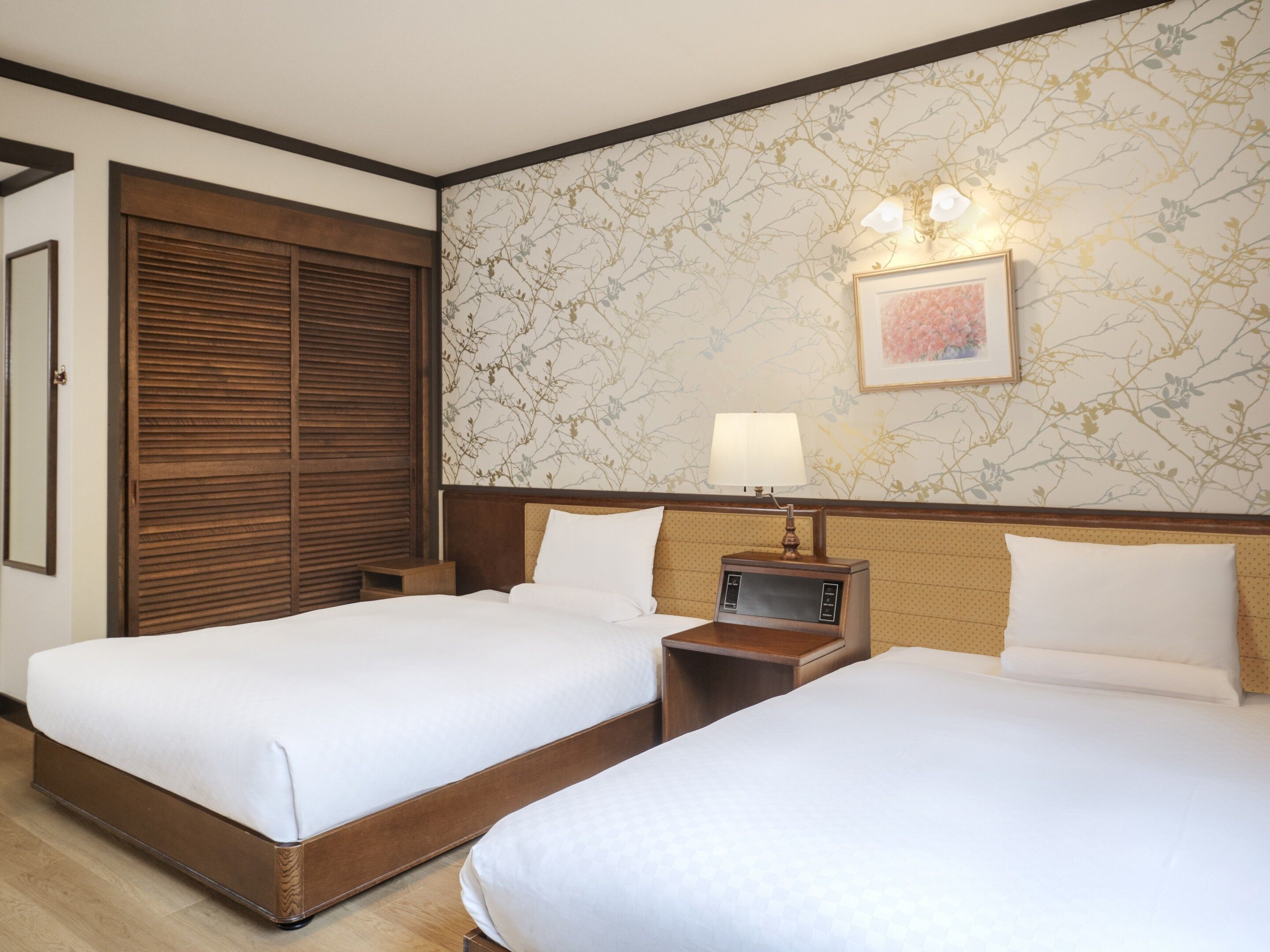 Een hotelkamer met twee bedden, een houten garderobe, een wandlamp en bloemenbehang.
