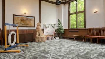 A room with a patterned carpet, wooden benches, a framed painting, and a window with a view of trees.
