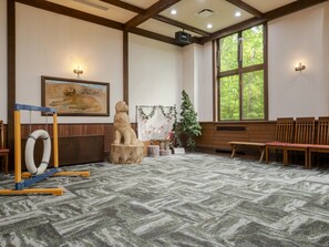 A room with a patterned carpet, wooden benches, a framed painting, and a window with a view of trees.