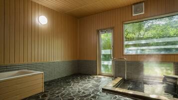 A traditional Japanese-style bath with a stone floor, wooden walls, and a large window.