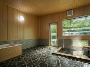 Un bain traditionnel de style japonais, avec un sol en pierre, des murs en bois et une grande fenêtre.