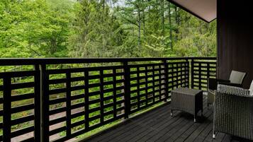 A wooden deck with a black railing, a wicker sofa, and a view of a forest.